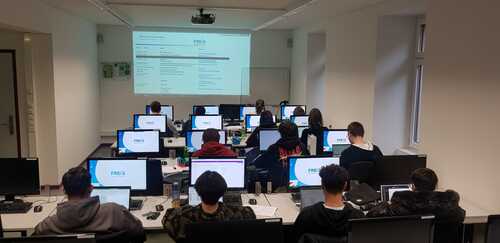 Klasse mit Lernenden der kaufmännischen Lehr im Schulzimmer hinter Computern