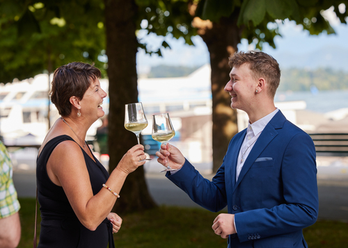 Zwei Angehörige von Diplomandinnen stossen mit einem Glas Wein am See an